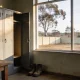 A depot smoko room at the end of a shift, a stainless steel kettle on a worn timber table, an open grey locker with work boots below and a high window onto a dry Australian yard
