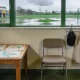 The entry area of an Australian early learning centre: children's paintings drying on a low table, a chair and a row of plain bags and hats on hooks, a wet playground beyond the window