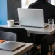 A person seen from behind working on a laptop at a cafe table, its screen facing away, with a coffee, a glass of water and a phone beside it