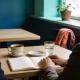 Two people in conversation at a cafe table with coffee, water and an open notebook of blank pages between them