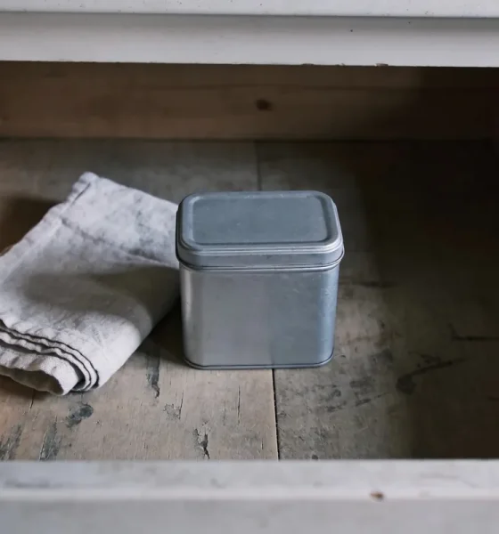 An open kitchen drawer in an Australian home holding a plain lidded tin and a folded cloth, in soft winter morning light