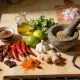 A kitchen bench spread of ingredients from several cuisines, with dried and fresh chillies, limes, garlic, ginger, coriander, a stone mortar and a jug of oil