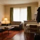 A furnished short-stay unit with a small sofa, dining table and kitchenette, a suitcase by the door and coats on hooks, seen from the doorway