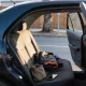 An open rear car door with a jacket, canvas bag and phone left on the back seat, on a quiet suburban street in the afternoon