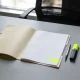 An open folder of blank pages on an office desk with a pen, highlighter, glasses, mug, plant and closed laptop in daylight