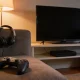 An Australian living room in the evening with a plain games controller on the couch, a headset on the armrest and a dark television above a plain console, lit by a warm lamp
