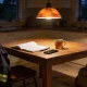 A kitchen table in the evening with an open notebook of blank pages, a pen, a phone and a mug of tea, a hi-vis work jacket over the chair and a bag on the floor
