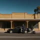 A plain sedan at the kerb of a country town shopfront with its rear door held open, a passenger with a suitcase walking towards it
